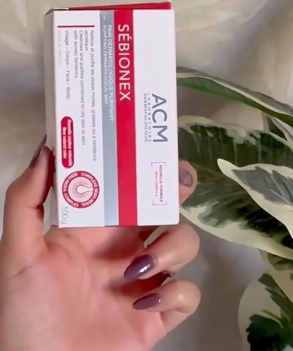 Hand holding a box of Sebionex ACM product with a plant in the background