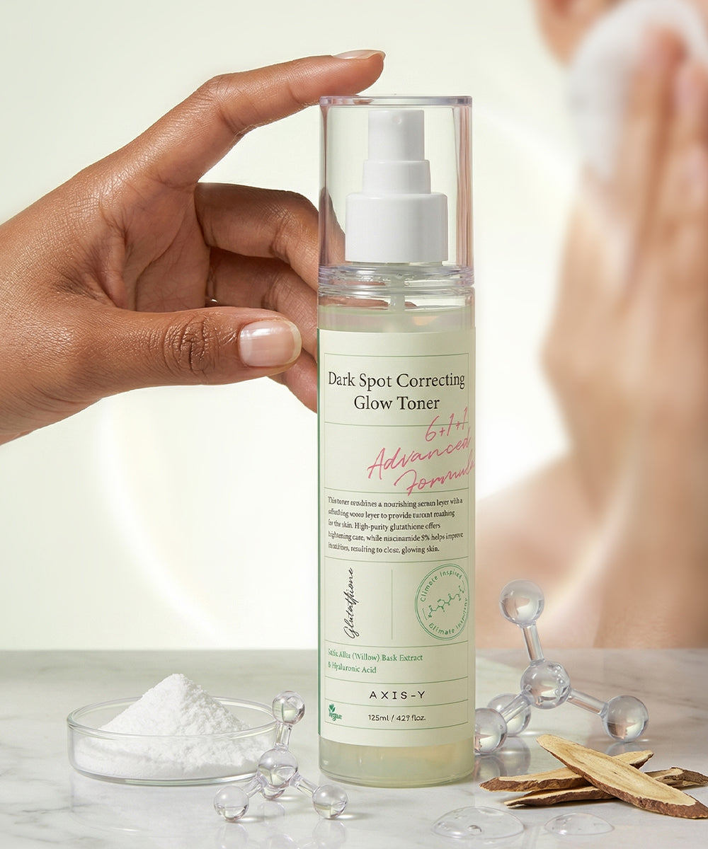 A bottle of AXIS-Y Dark Spot Correcting Glow Toner held by a hand with a blurred background.