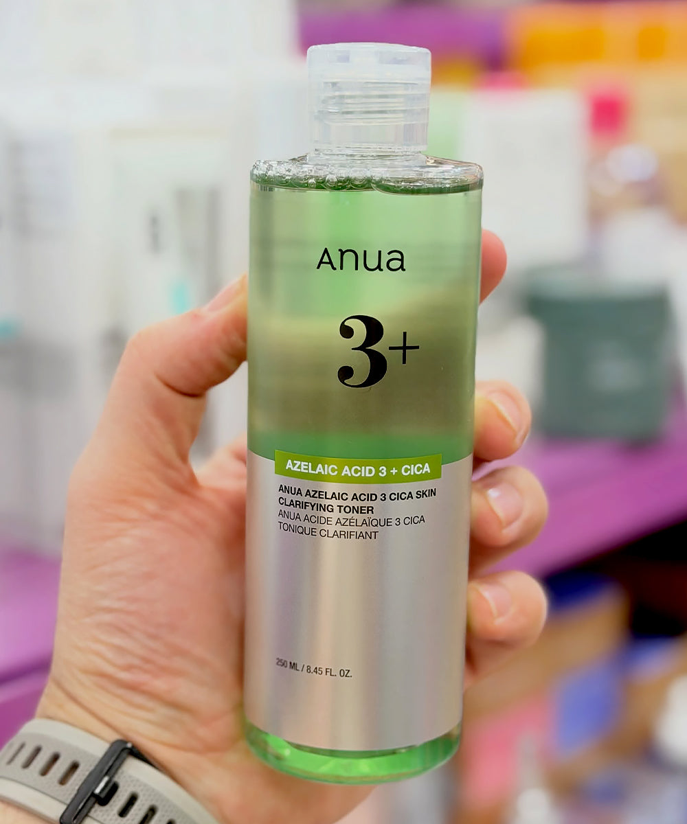 A real-life perspective showing a hand holding a 250ml bottle of Anua Azelaic Acid 3 + Cica Toner in a retail environment, showcasing the product's scale and translucent green tint
