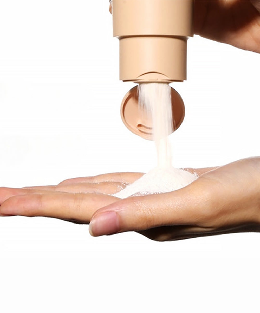 Hand holding a beige container with cream being dispensed onto the palm against a white background