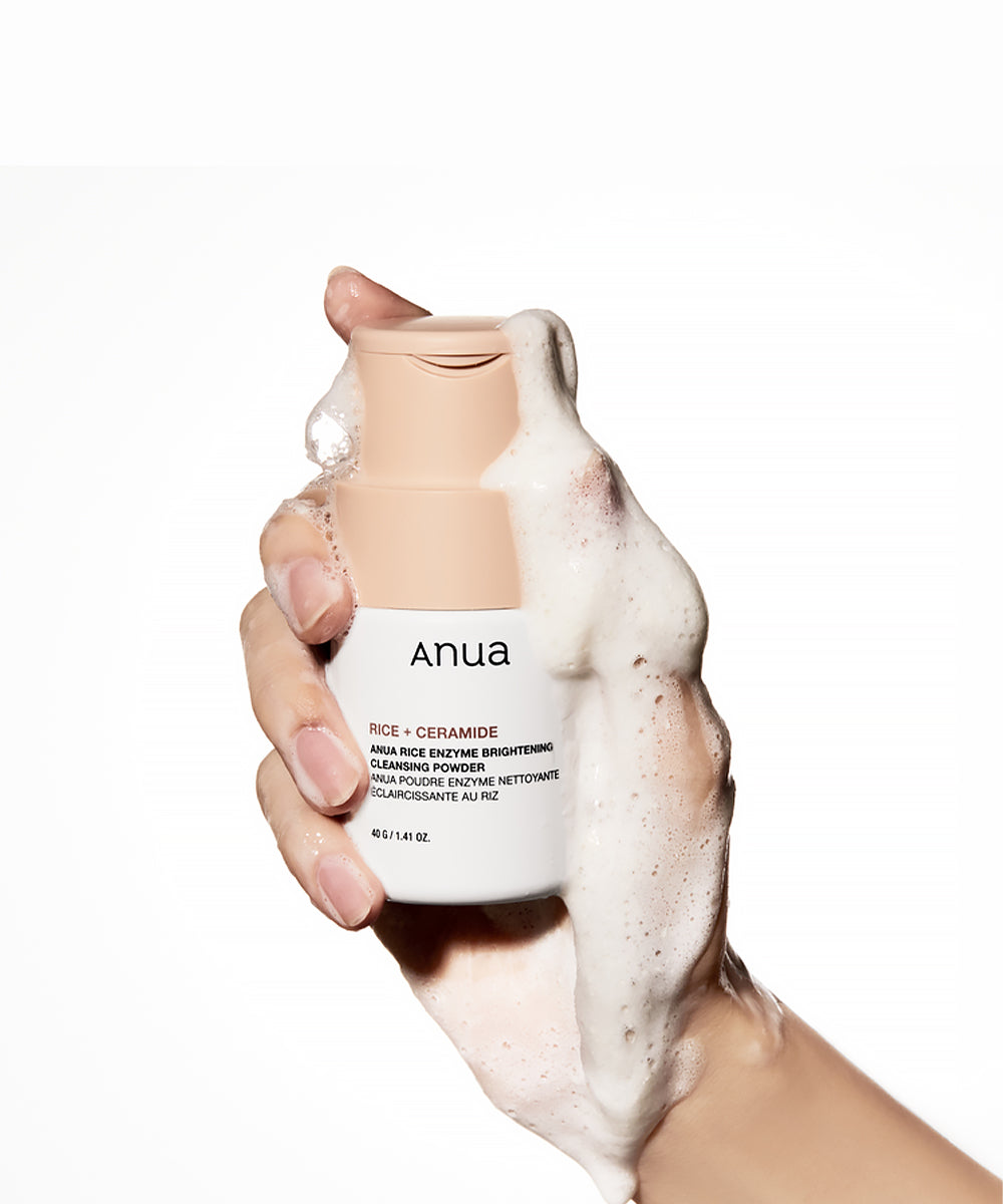 Hand holding a bottle of anua skincare product with foam on a white background