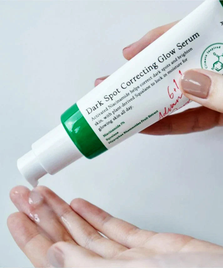 Hand holding a tube of dark spot correcting glow serum with visible text on a light background