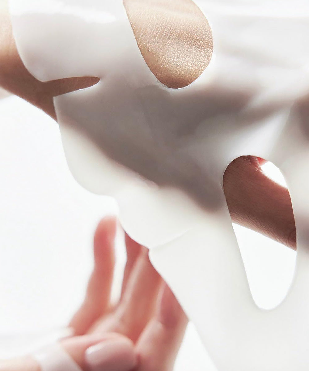 Close-up of a hand holding a white mask with a blurred background