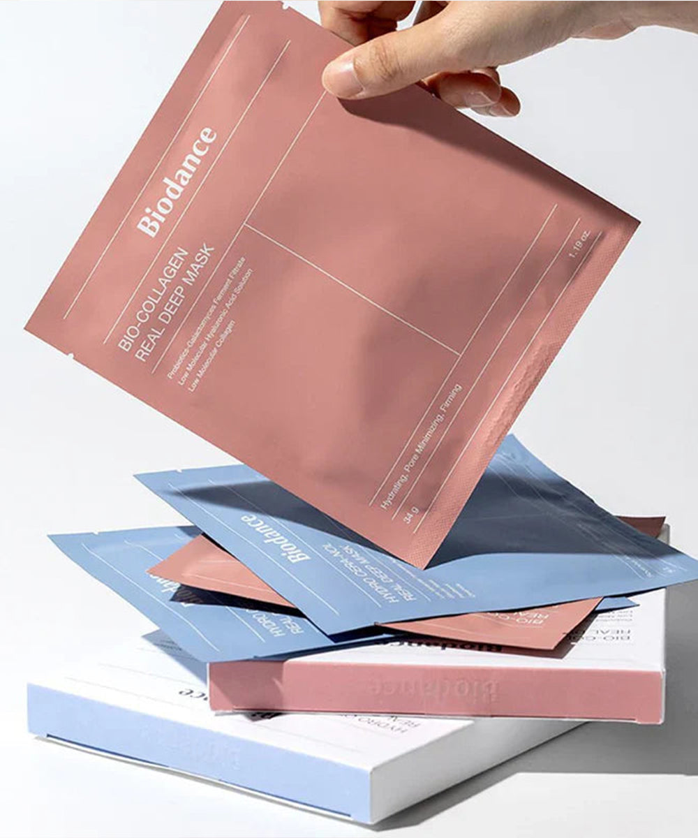 Hand holding a stack of Biodance Real Deep Mask packaging on a light gray background