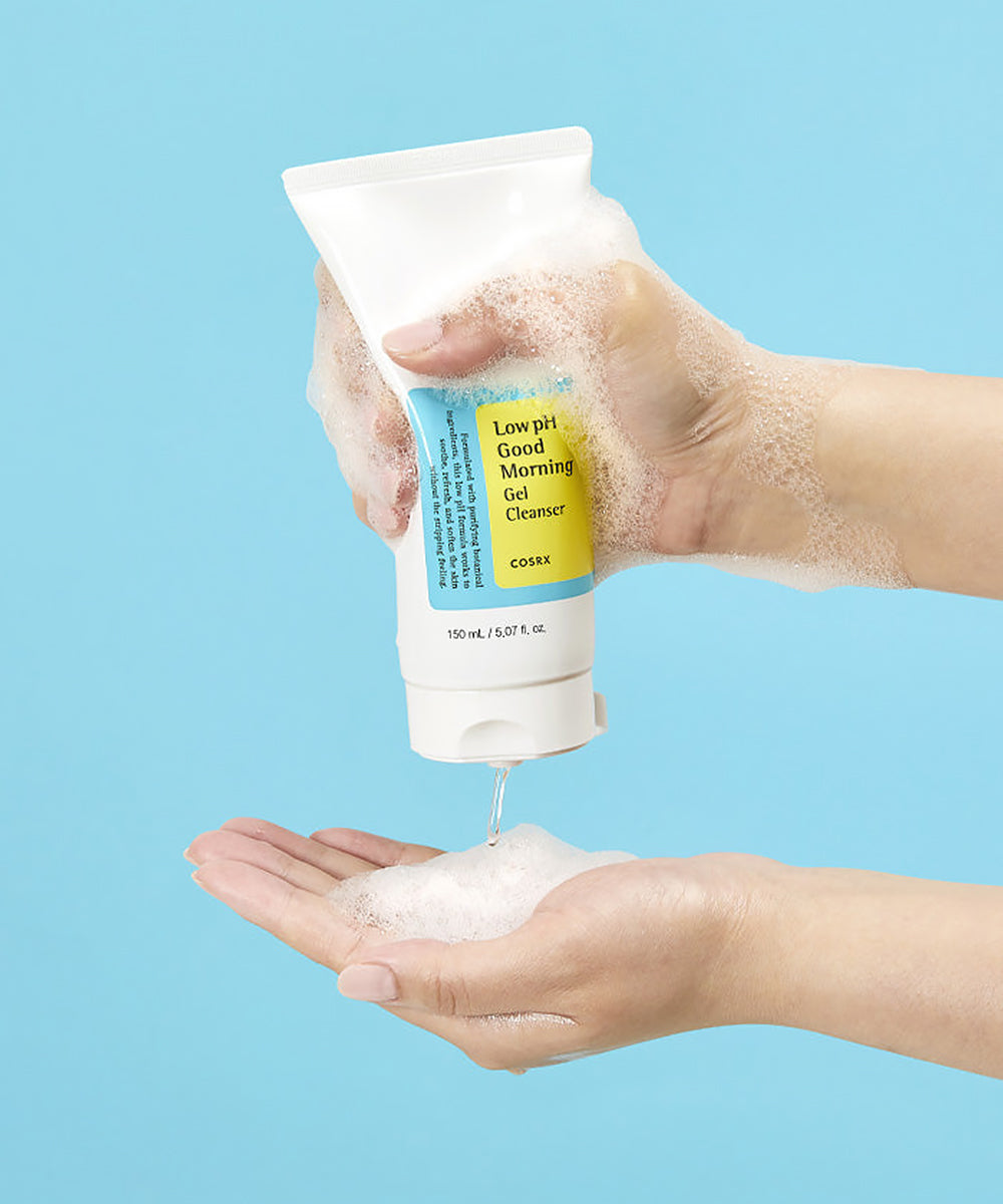 Hand holding a tube of 'Good Morning' cleanser with foam being dispensed on a blue background