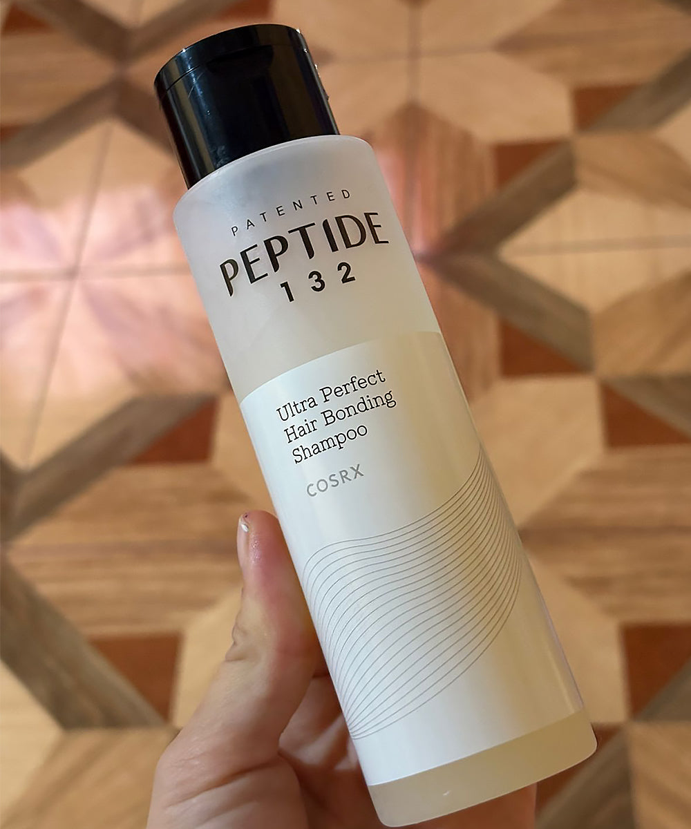 CosRX Peptide 132 shampoo bottle held in a hand with a geometric patterned background