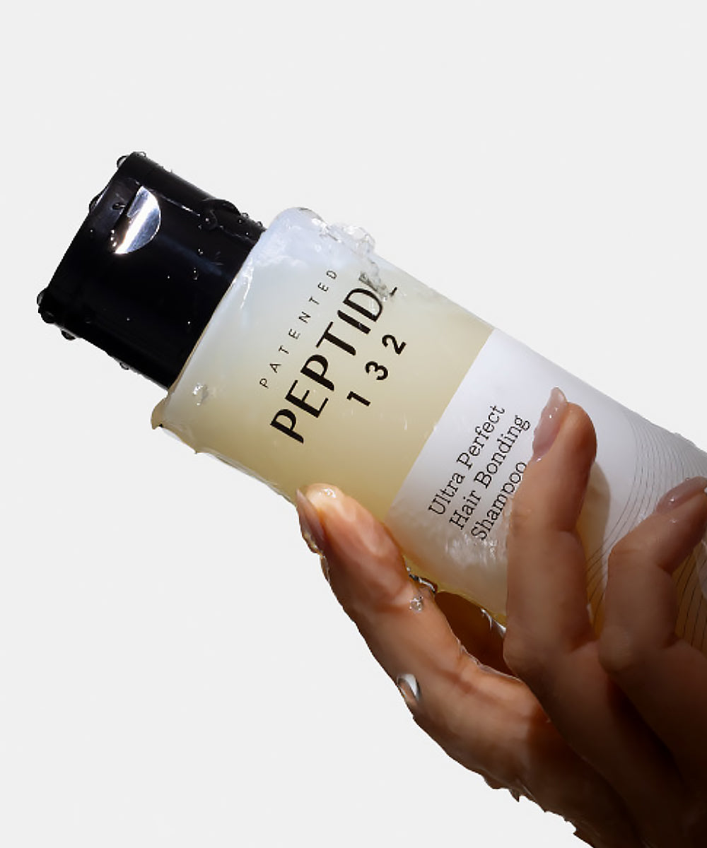 Hand holding a bottle of 'Peptide 132' shampoo with a white background