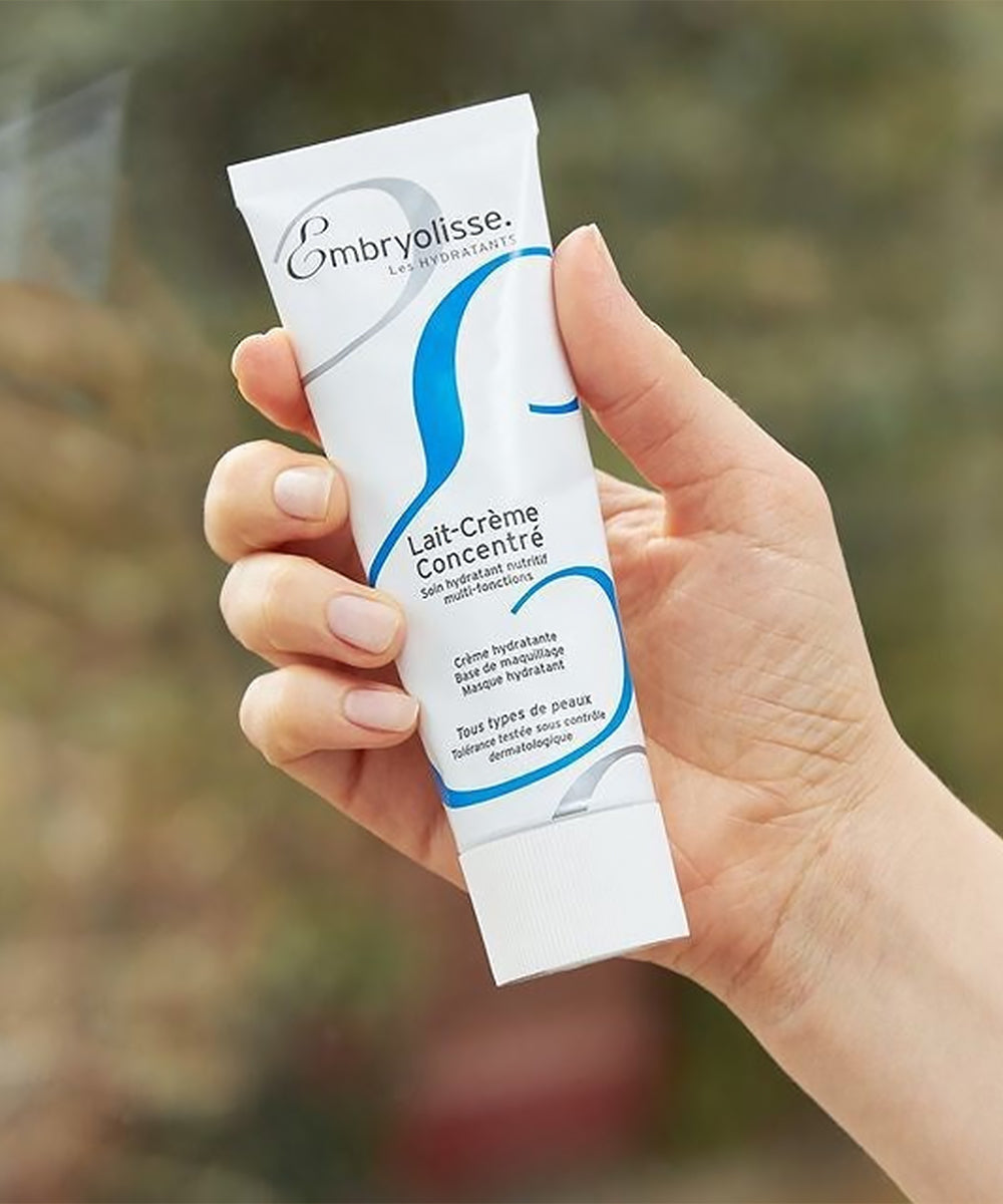 Hand holding Embryolisse skincare product with a blurred natural background
