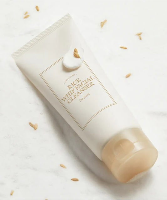 White rice facial cleanser bottle on a light background with scattered rice grains.