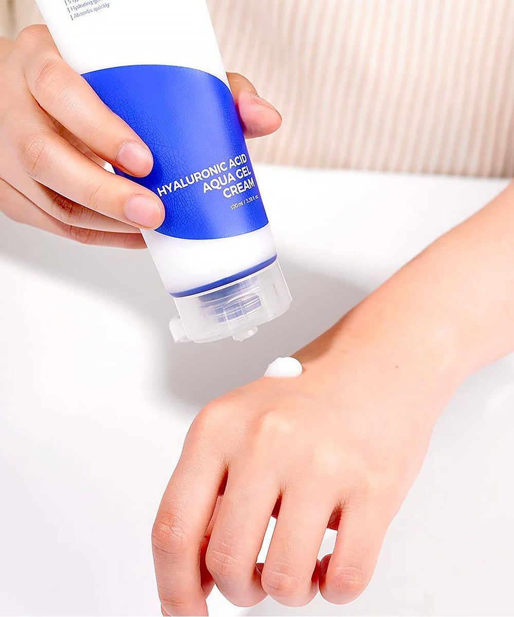 Person applying a blue and white bottle of cream to their wrist.