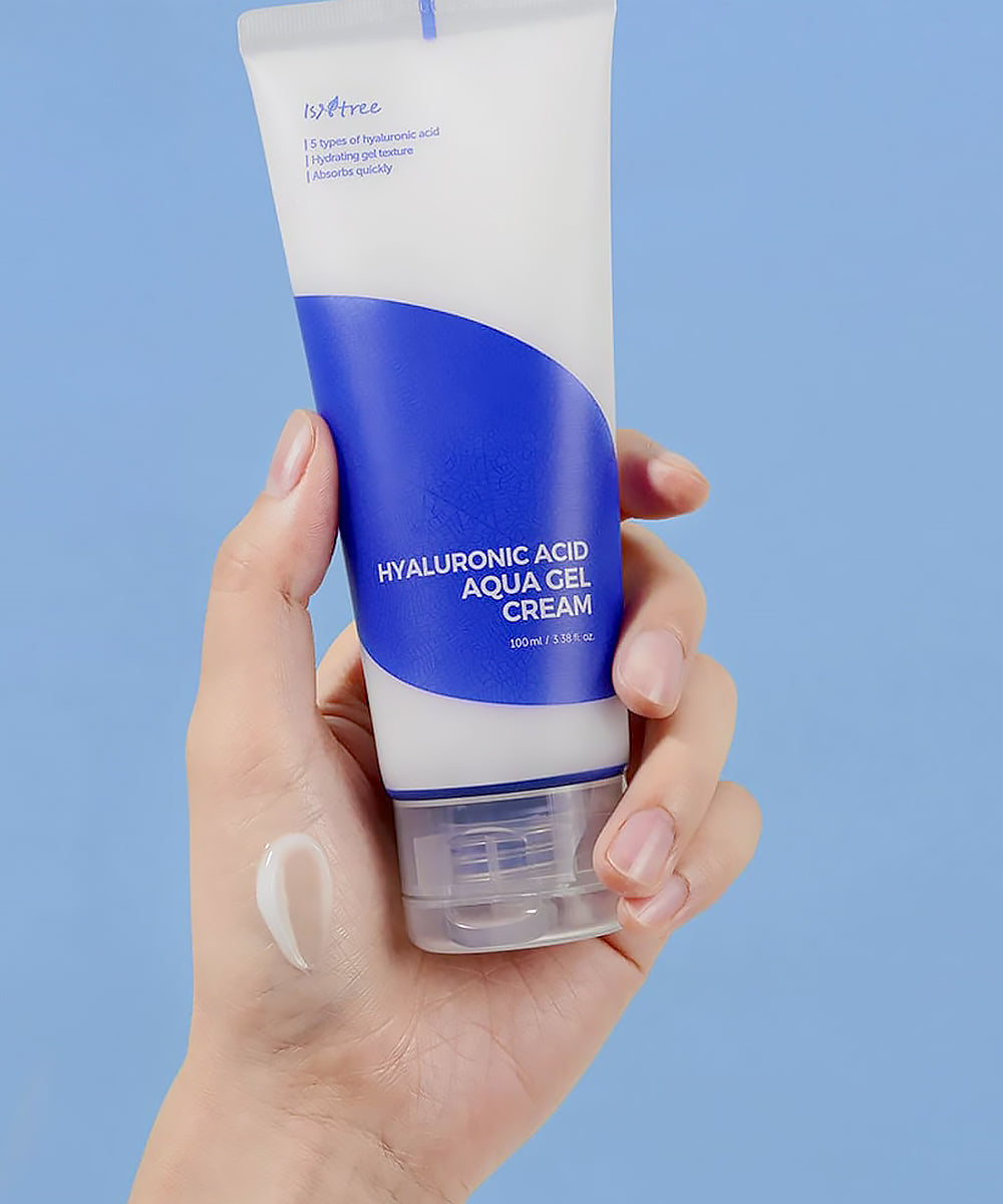 Hand holding a tube of hyaluronic acid aqua gel cream against a blue background