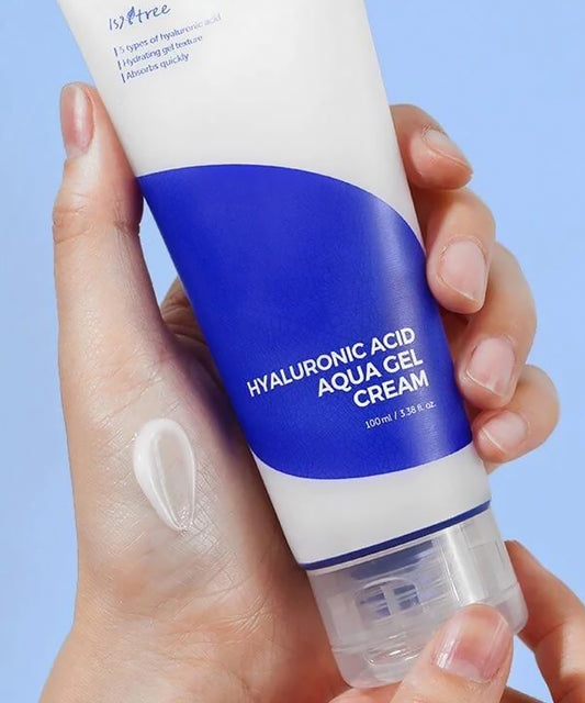 Hand holding a tube of hyaluronic acid aqua gel cream against a light blue background
