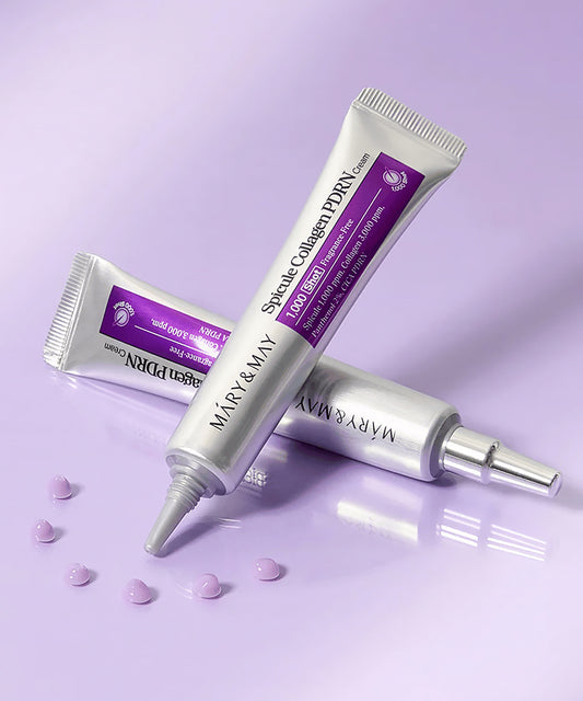 A lifestyle shot showing two silver tubes of Mary & May Spicule Collagen PDRN Cream on a lavender surface, surrounded by small purple cream droplets to showcase product texture