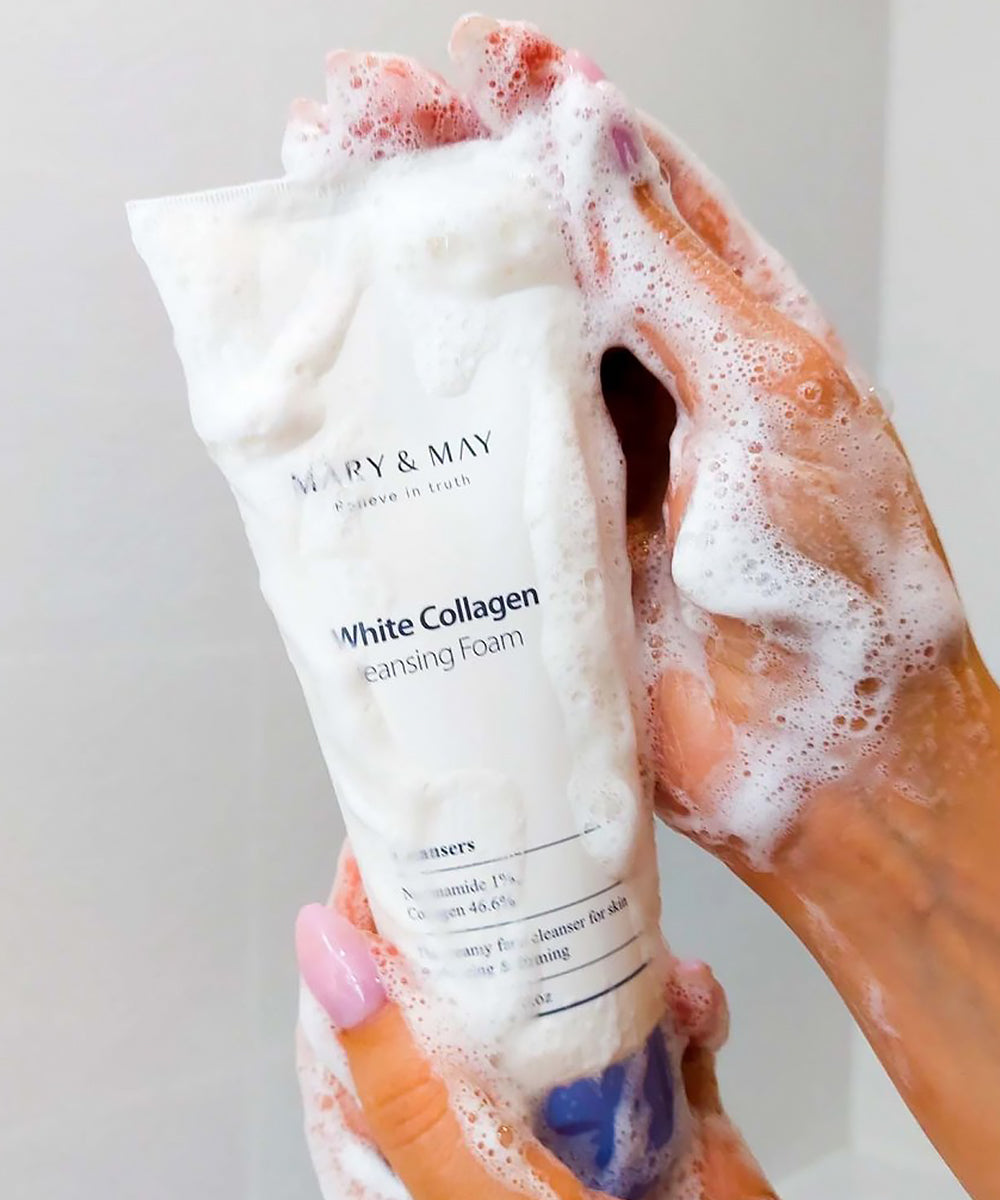 White Collagen Cleansing Foam tube with foam on a hand against a neutral background