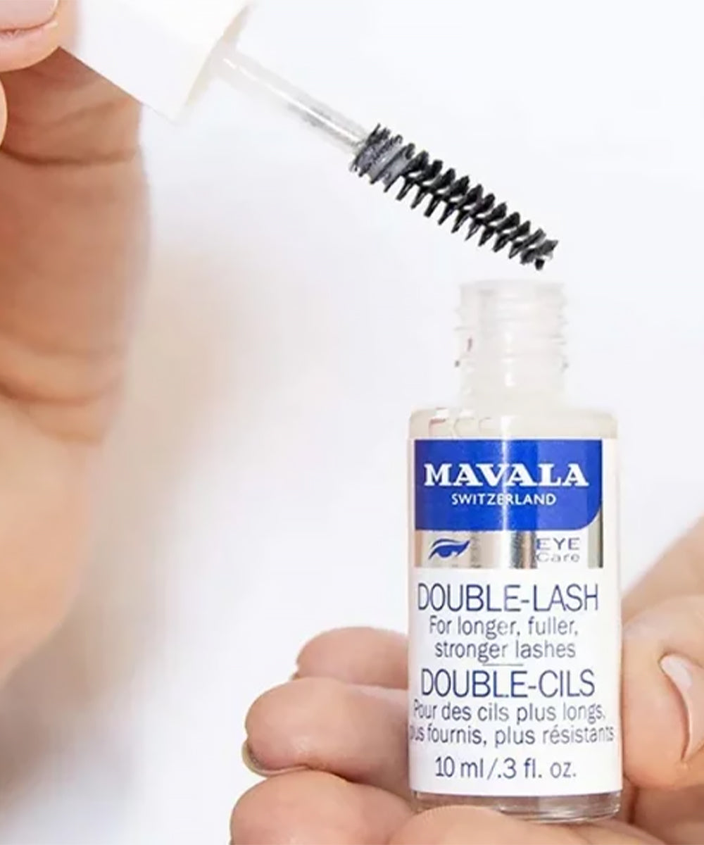 Mavala Double-Lash eyelash serum bottle with applicator held by a hand against a white background