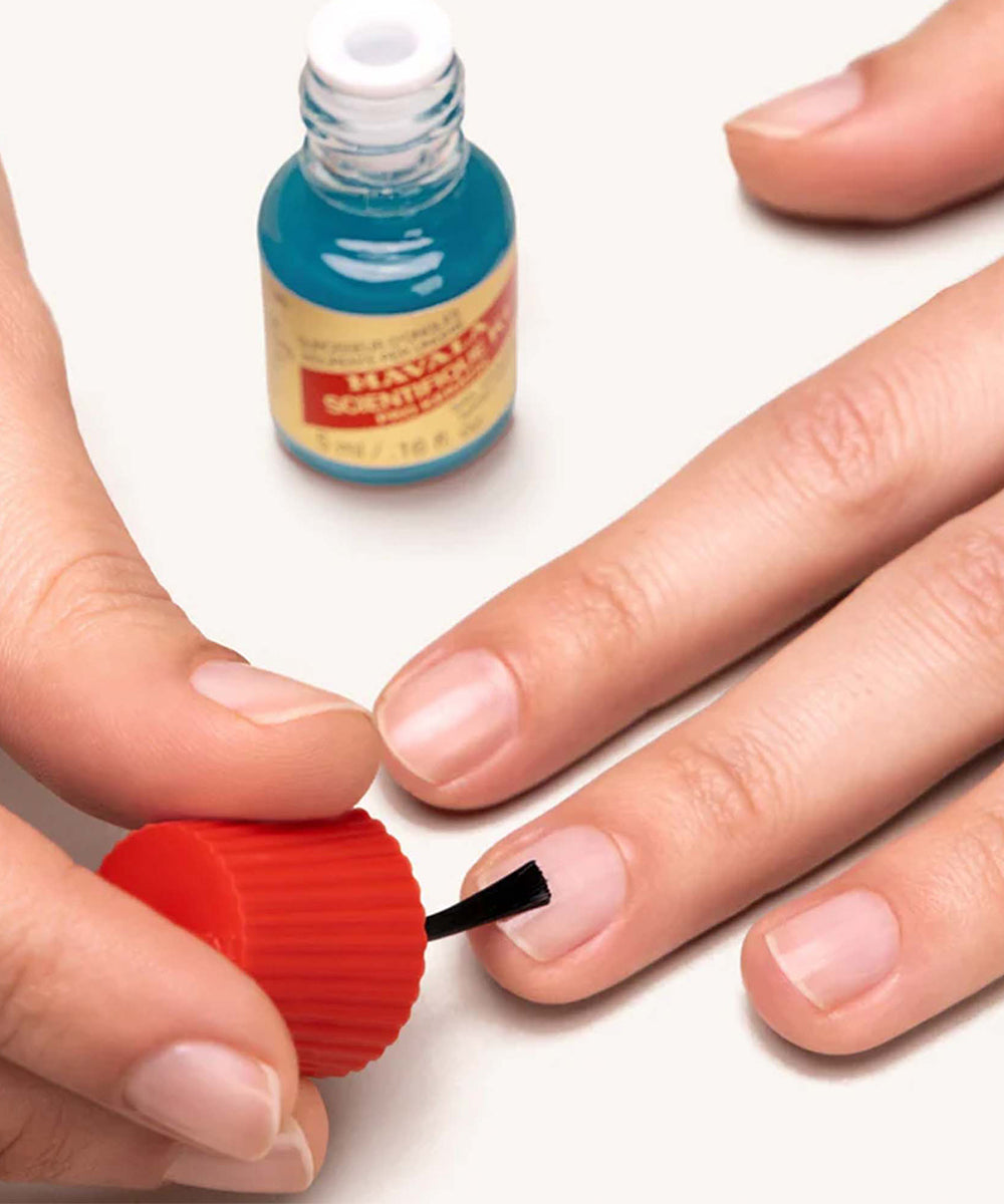 Person applying nail polish to their fingernail with a bottle of nail polish in the background.