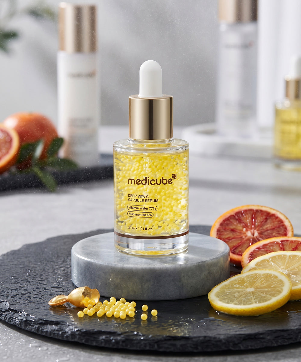 Lifestyle shot of the Deep Vita C Capsule Serum on a grey marble pedestal, surrounded by fresh slices of orange and lemon to visualize the high Vitamin C content