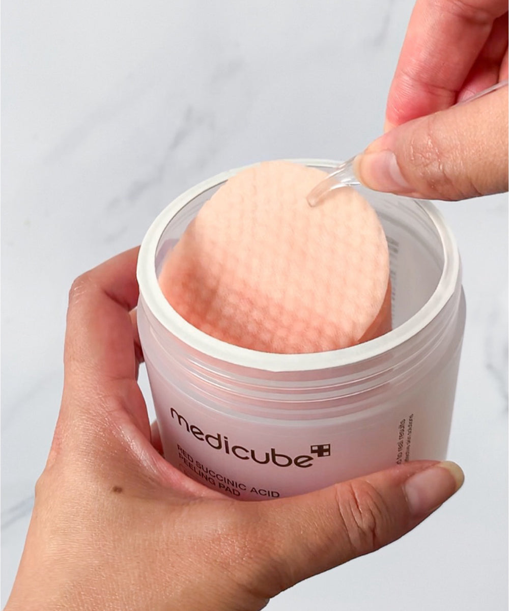 Person using a Medicube skincare product with a cotton pad on a plain background