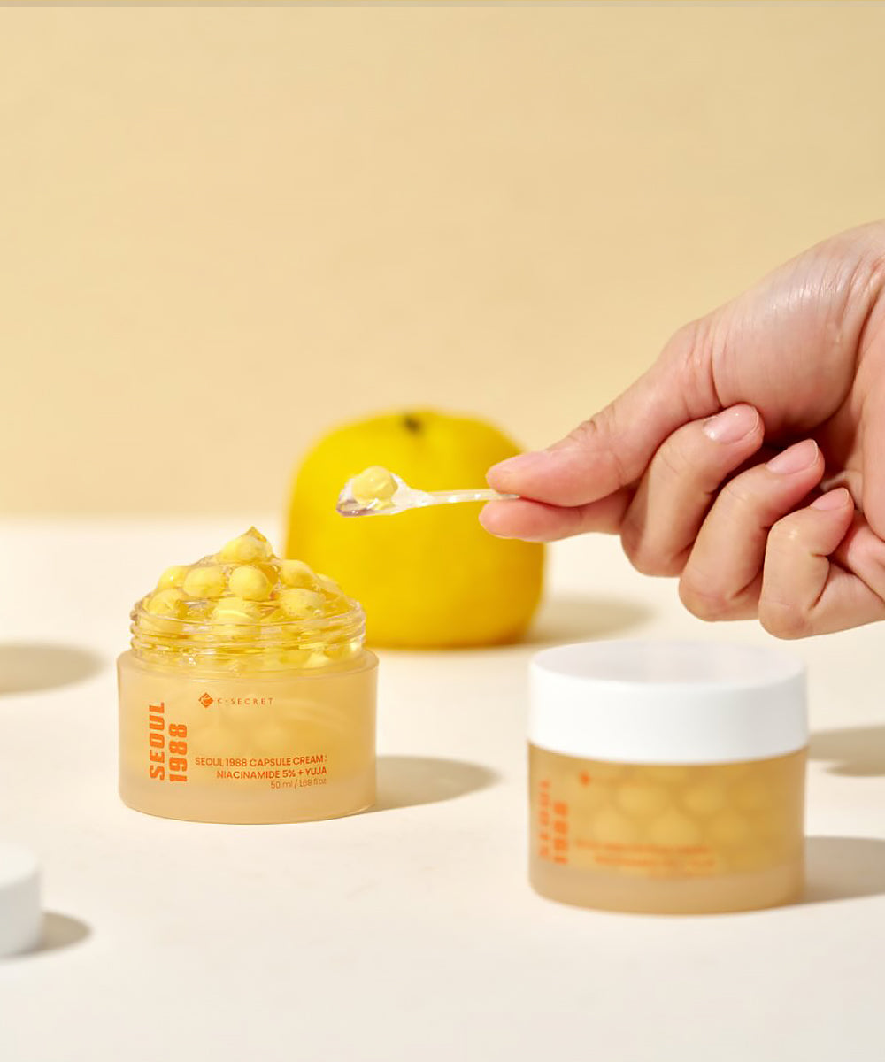 Hand holding a dropper over a jar of cream with a yellow background