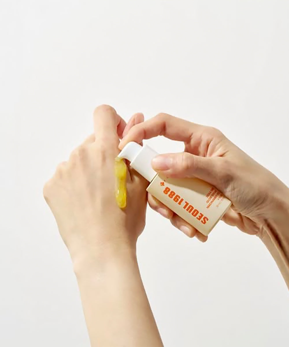 Person applying a yellow substance from a tube labeled 'SEOUL 1988' on a white background