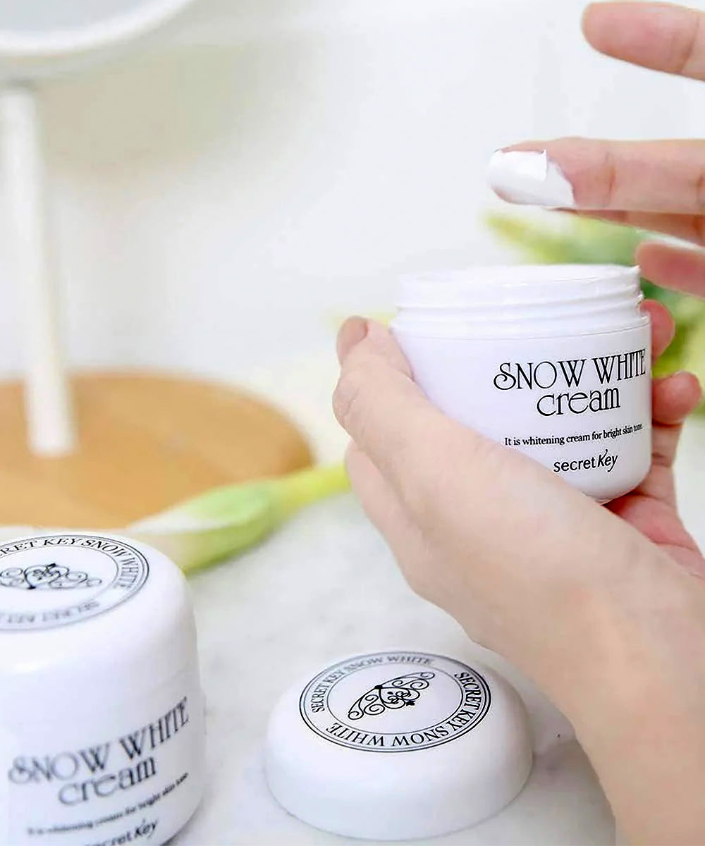 Hand holding a jar of Snow White cream with a blurred background