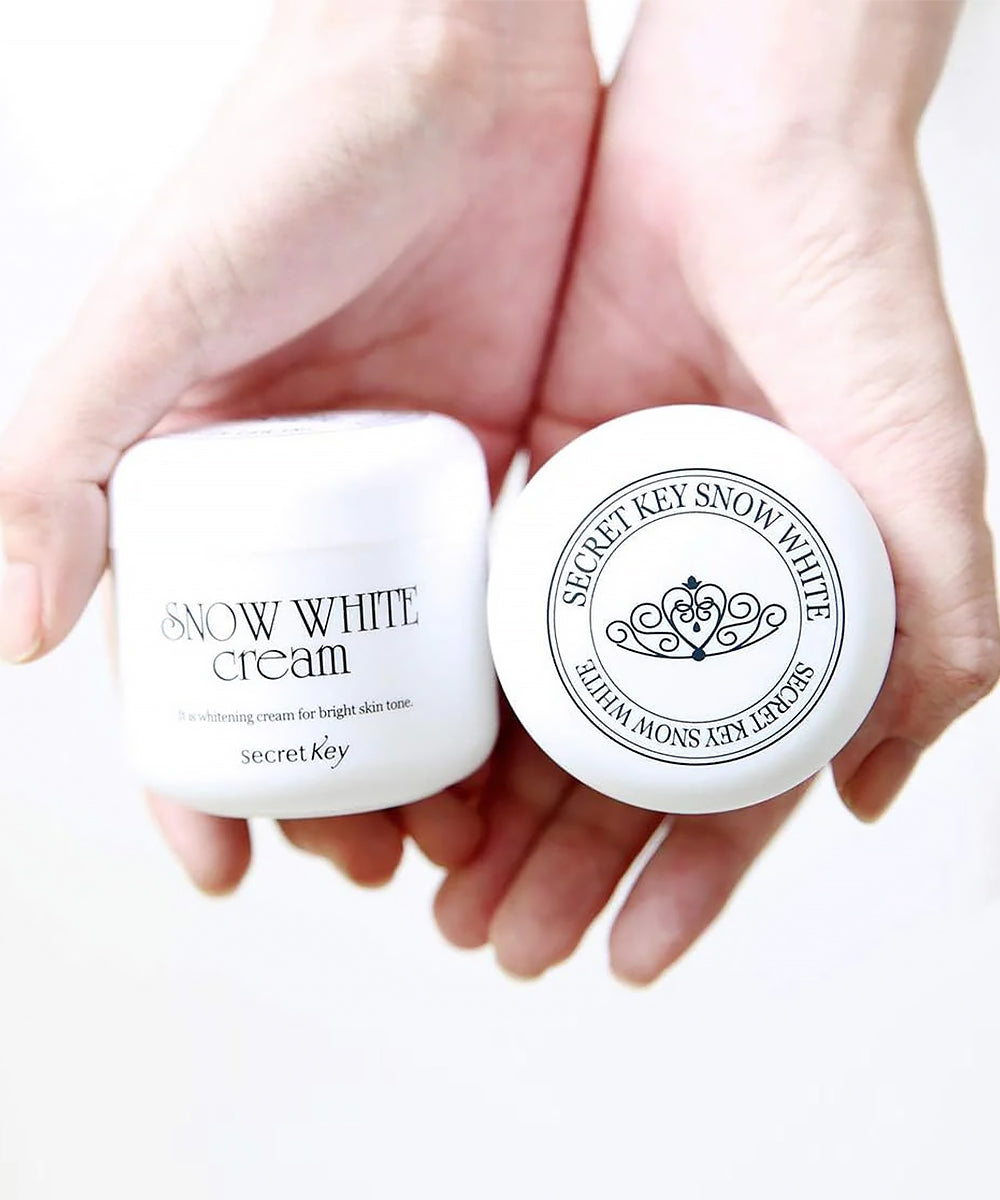 Two containers of Secret Key Snow White Cream held in hands against a white background