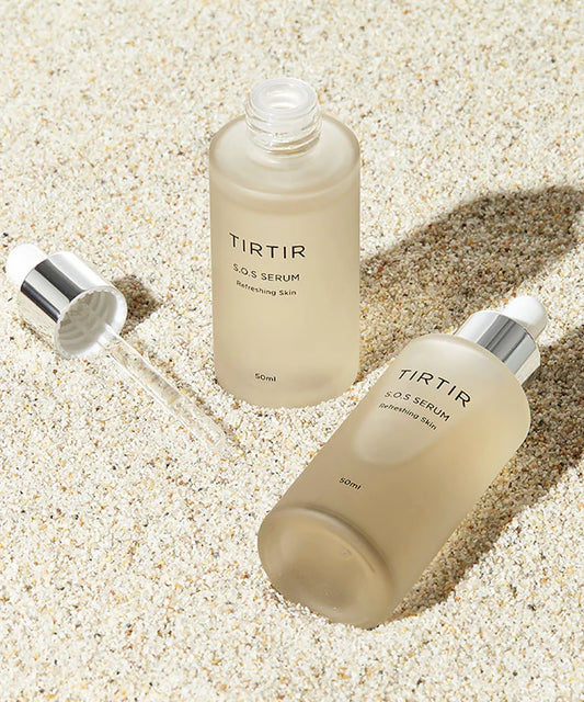 Two bottles of TIRTIR SOS Serum and a glass dropper displayed on a light, sandy surface to evoke a clean and natural aesthetic