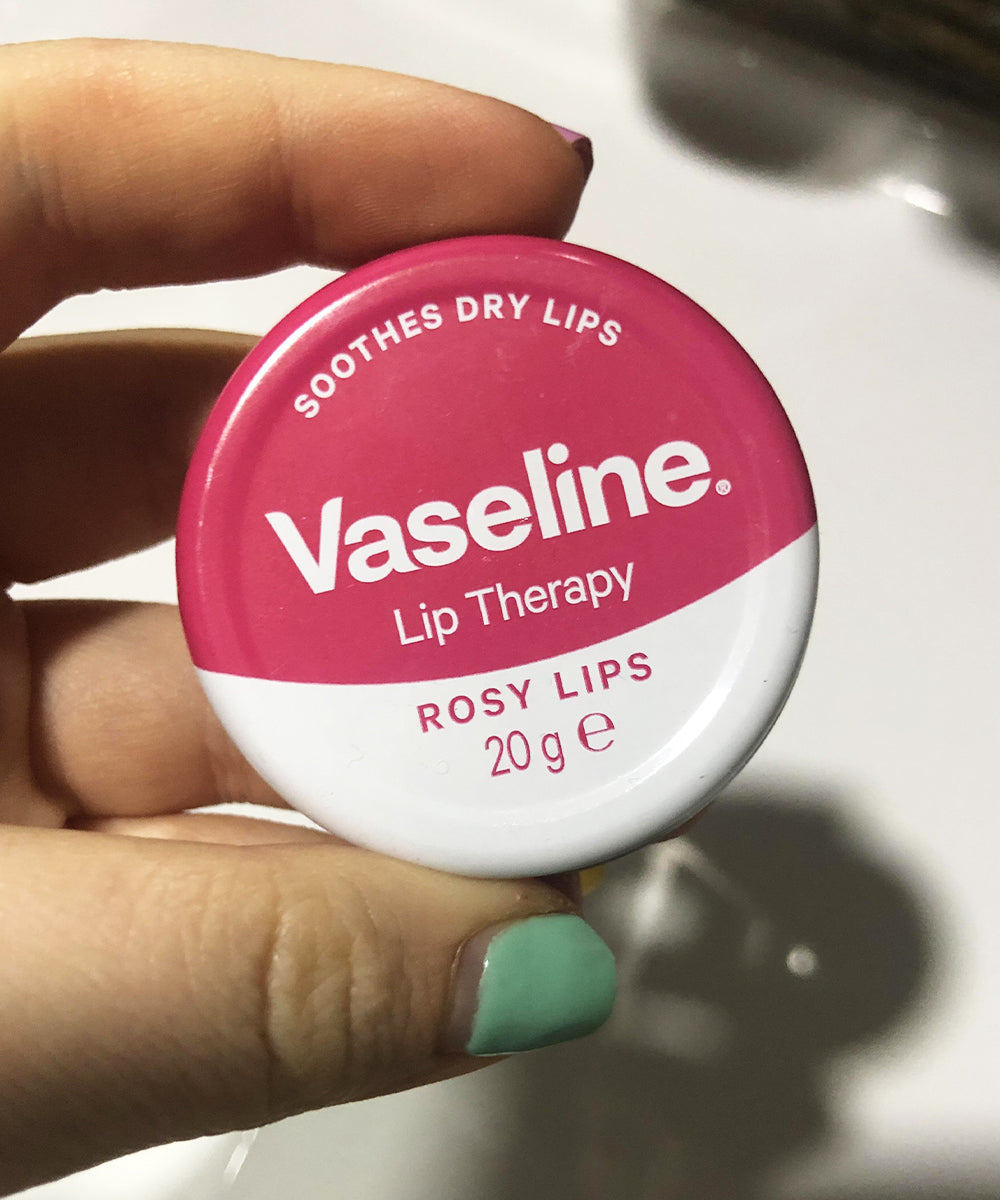 Vaseline lip therapy container held by a hand with green nail polish.