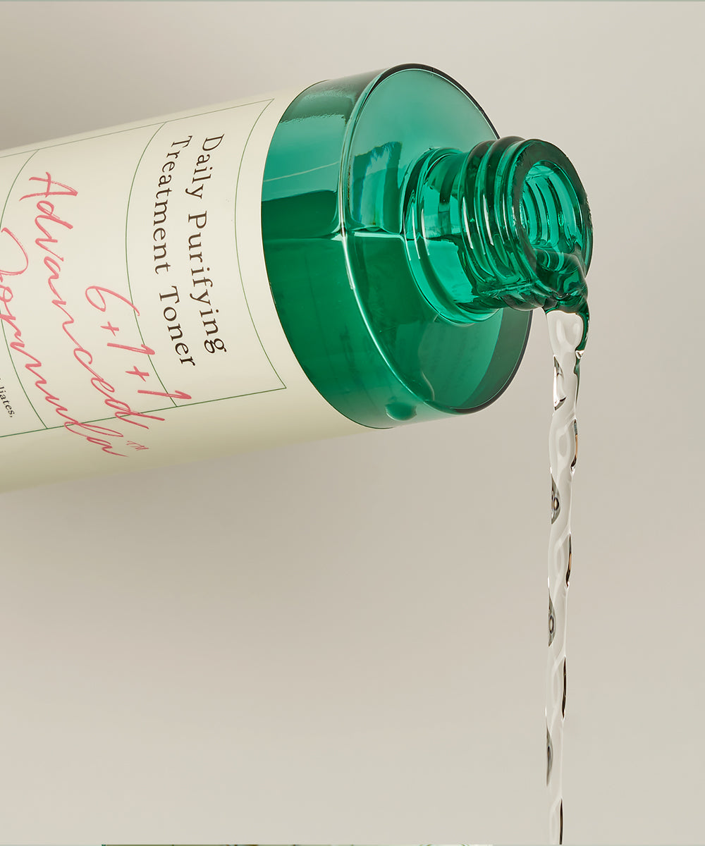 Green bottle of skincare product with clear liquid being poured on a light gray background