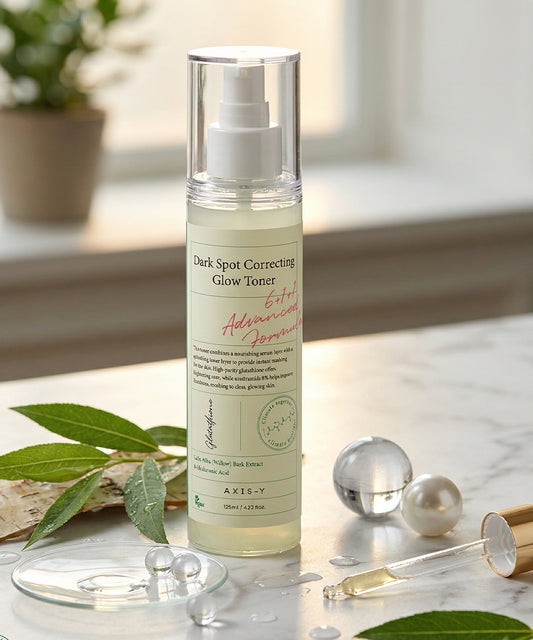 Skincare bottle labeled 'Dark Spot Correcting Glow Toner' on a marble surface with decorative elements.