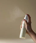 Hand holding a spray bottle with a beige background