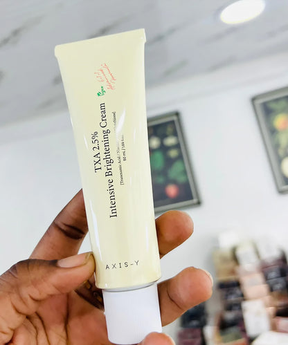 Hand holding a tube of AXIS-Y Intensive Brightening Cream with blurred background