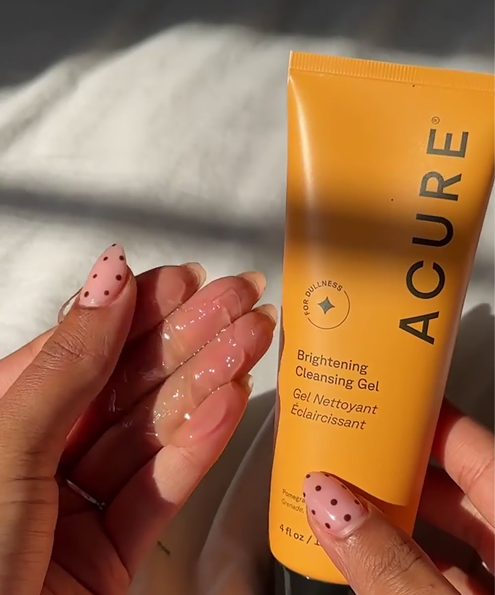 Hand holding a tube of Acure Brightening Cleansing Gel with a blurred background