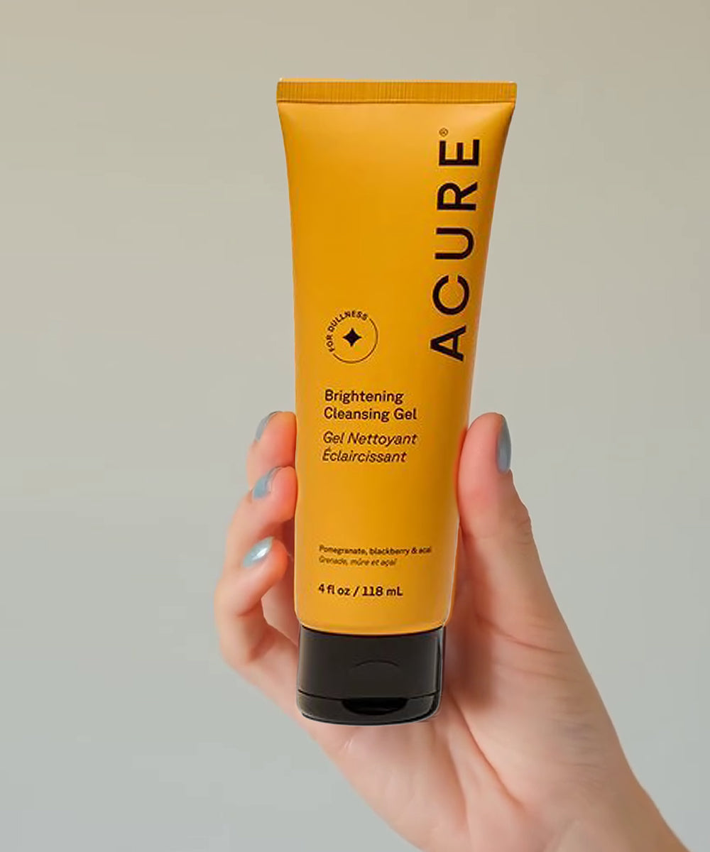 Hand holding a tube of Acure Brightening Cleansing Gel against a plain background