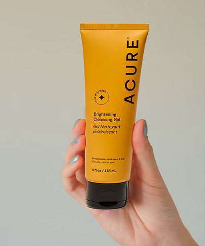 Hand holding a tube of Acure Brightening Cleansing Gel against a plain background