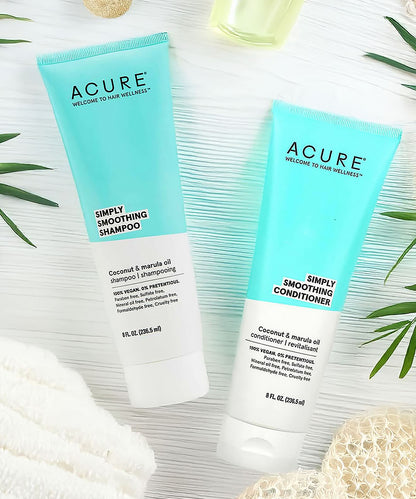 Acure Simply Smoothing Shampoo and Conditioner on a textured surface with green leaves.