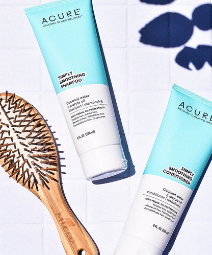 Acure Simply Smoothing Shampoo and Conditioner bottles with a wooden hairbrush on a light background