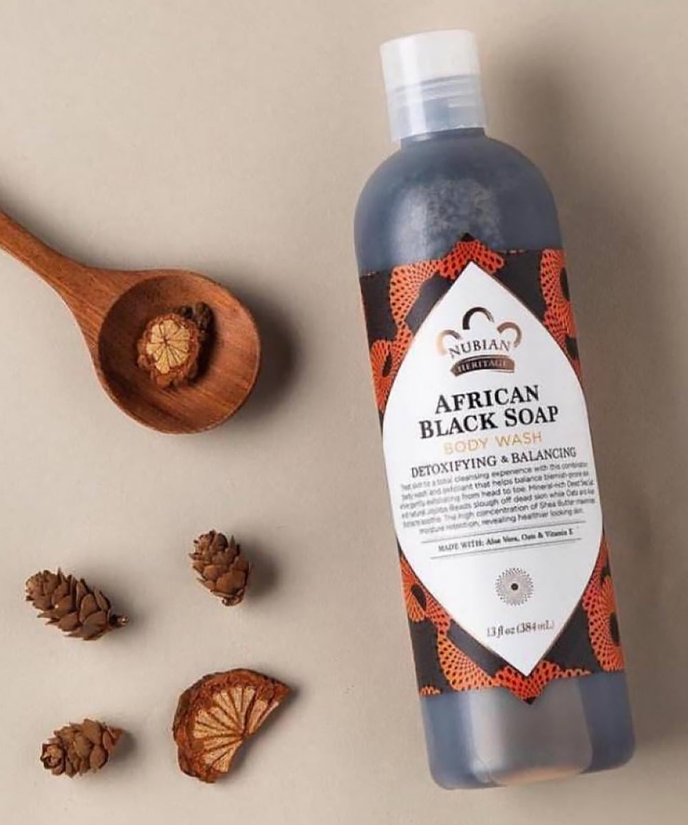 Nubian Heritage African Black Soap body wash bottle with wooden spoon and cones on beige background