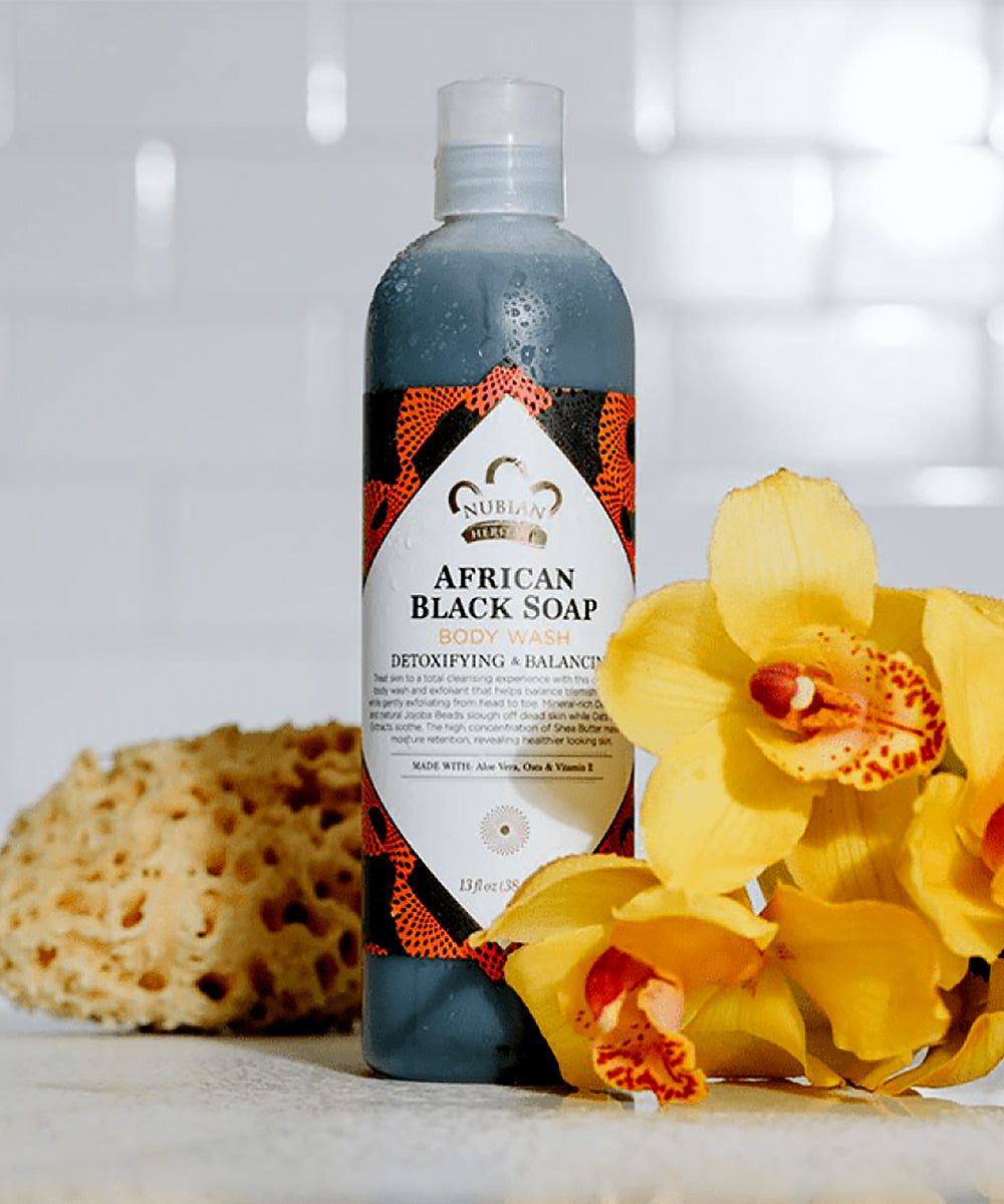 Bottle of African Black Soap with a yellow flower and sponge on a light background