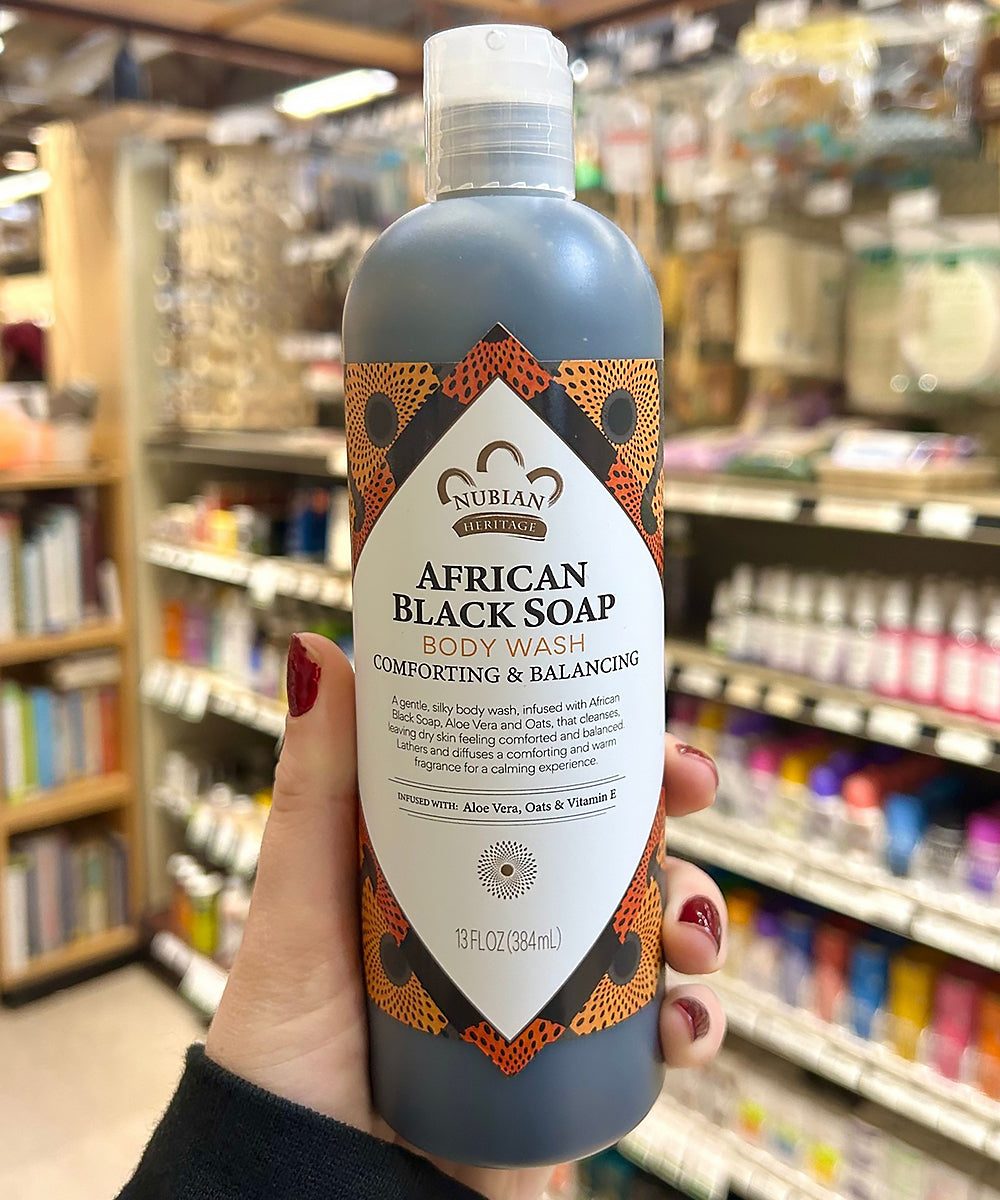 Person holding a bottle of Nubian Heritage African Black Soap Body Wash in a store setting.