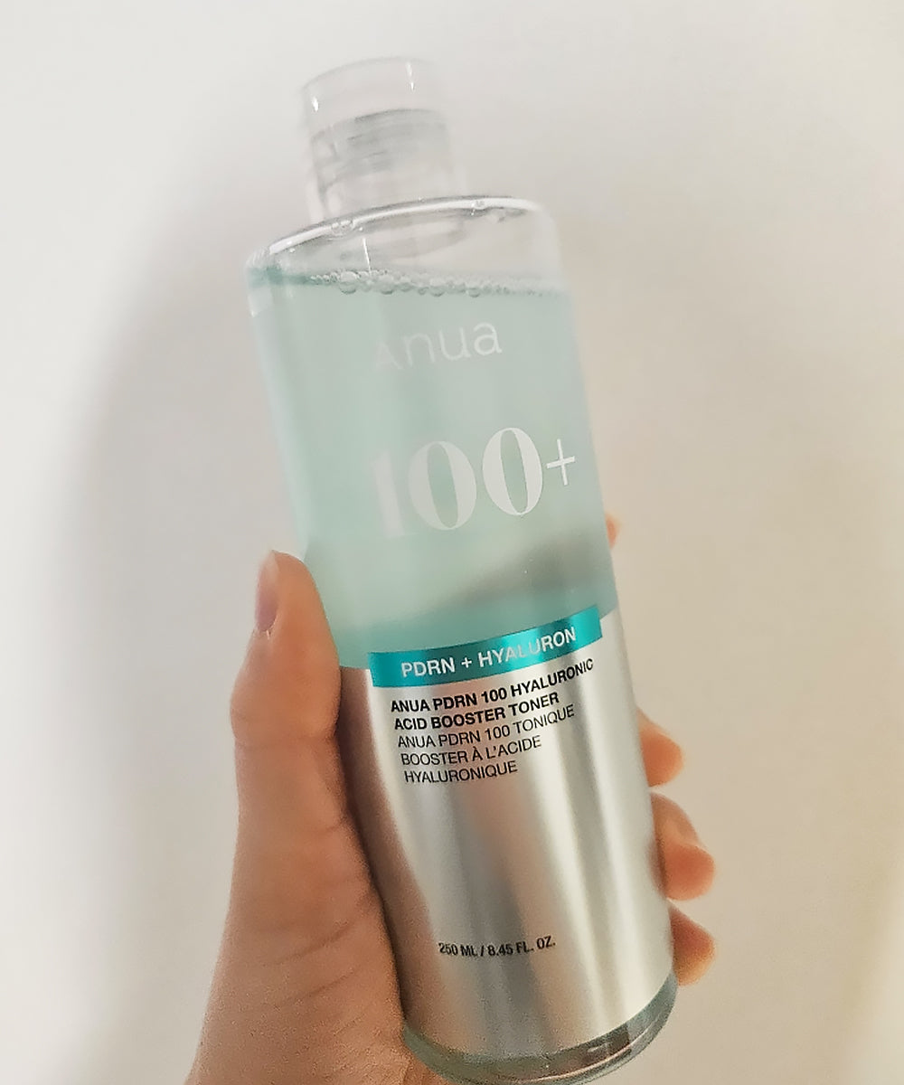 Hand holding a skincare bottle labeled 'Anua' with text on a white background