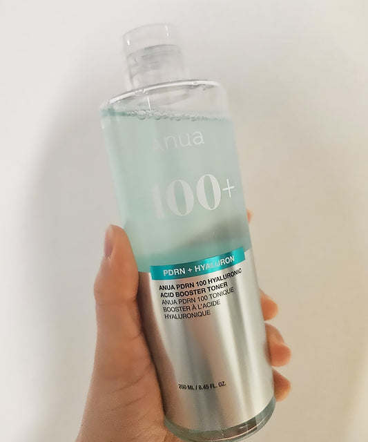 Hand holding a skincare bottle labeled 'Anua' with text on a white background