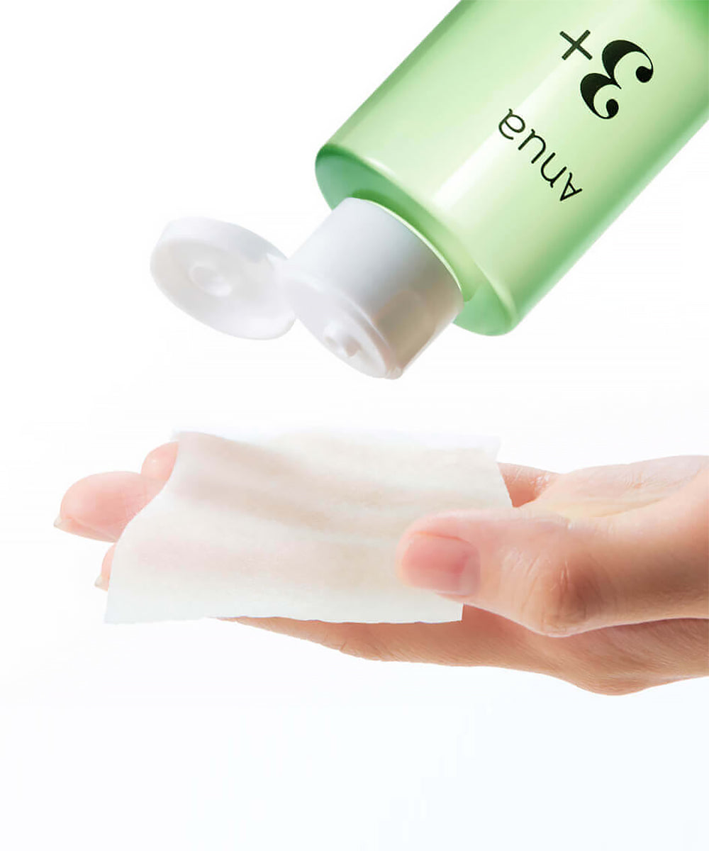 A close-up action shot of the Anua toner bottle being tilted to dispense product onto a white cotton pad held in a hand, illustrating ease of use