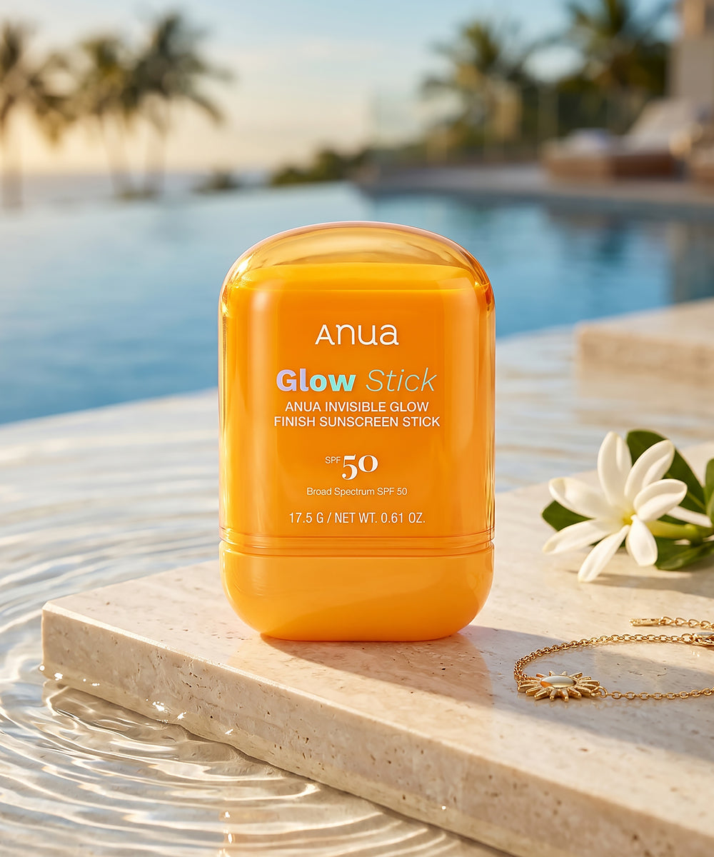 Anua Glow Stick sunscreen stick on a wooden surface with a pool and palm trees in the background