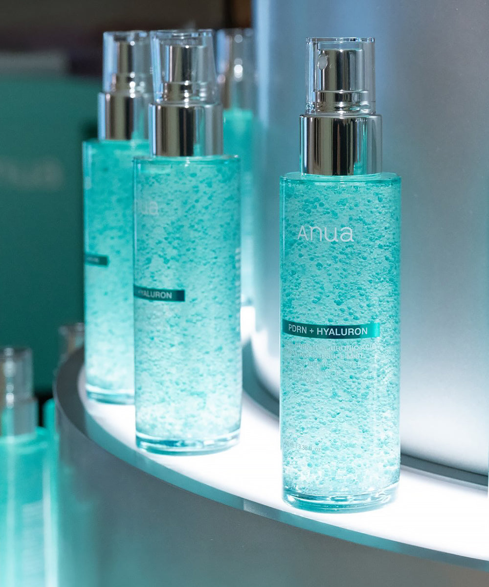 A row of Anua PDRN + Hyaluron Hydrating Capsule Mist bottles displayed on a lit shelf, highlighting the visually striking teal capsule texture