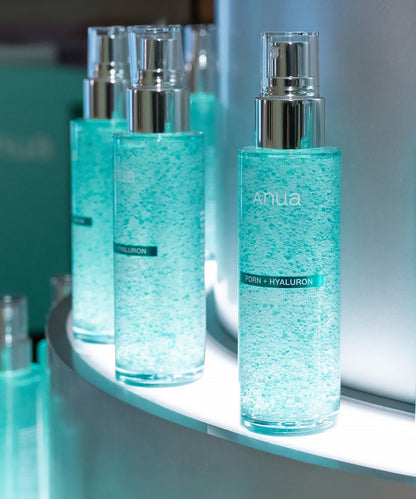 A row of Anua PDRN + Hyaluron Hydrating Capsule Mist bottles displayed on a lit shelf, highlighting the visually striking teal capsule texture