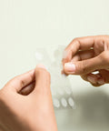 Hands holding a sheet of adhesive dots against a light background