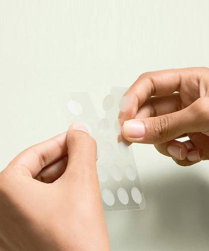 Hands holding a sheet of adhesive dots against a light background