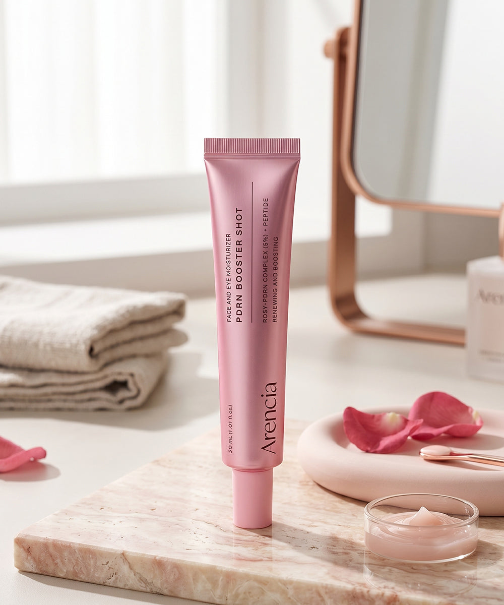 Lifestyle photography of the Arencia moisturizer on a marble vanity, surrounded by fresh rose petals and a small dish of the product, emphasizing its "Rosy-PDRN Complex."