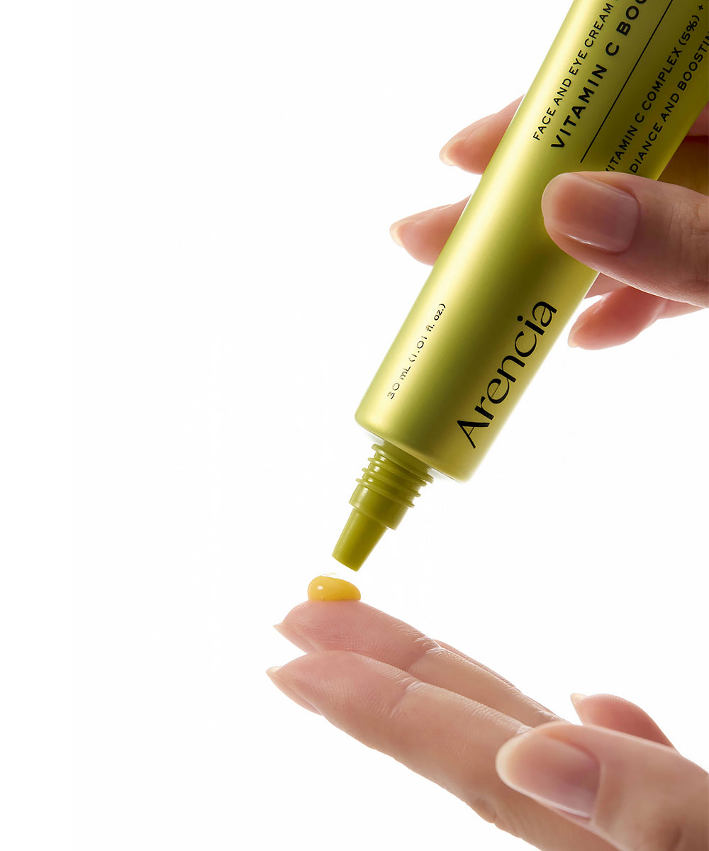 Hand holding a gold Arancia skincare product with a dropper on a white background